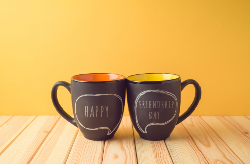 Cups knocking in cheers, one says 'happy' and the other with 'friendship day'