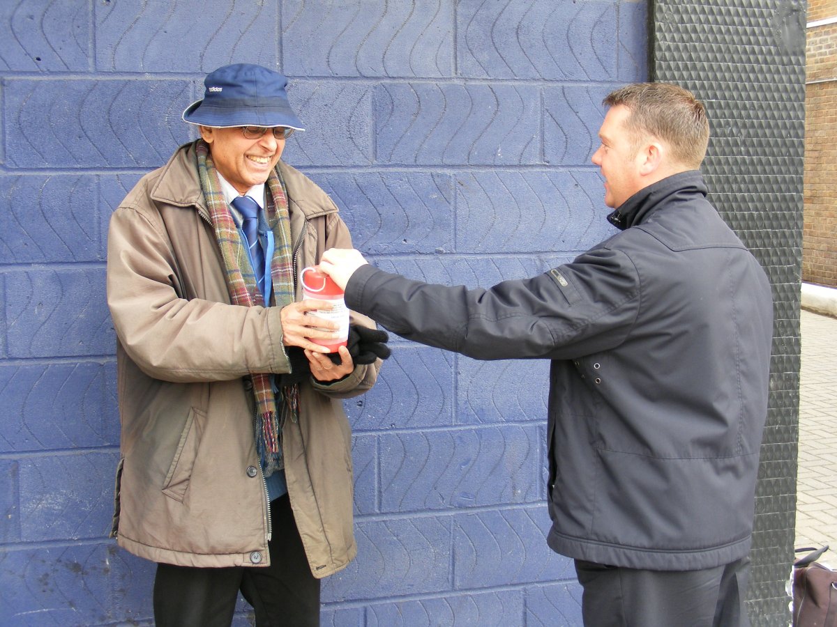man in a blue hat with a collection box and a man in black jacket making donation