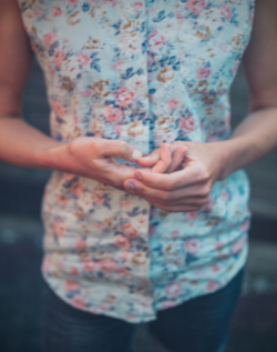 thin woman with a floral sleeveless blouse holding her hands nervously