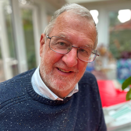 Photo of Sir John Battle, KCSG, wearing blue sweater, shirt and glasses