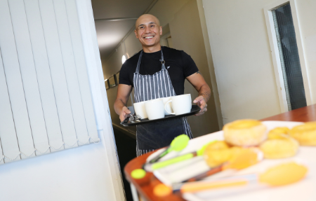 Smiling bald man in apron carrying tray of mugs