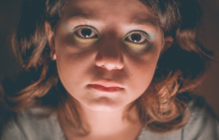 A sad looking little girl darkly lit