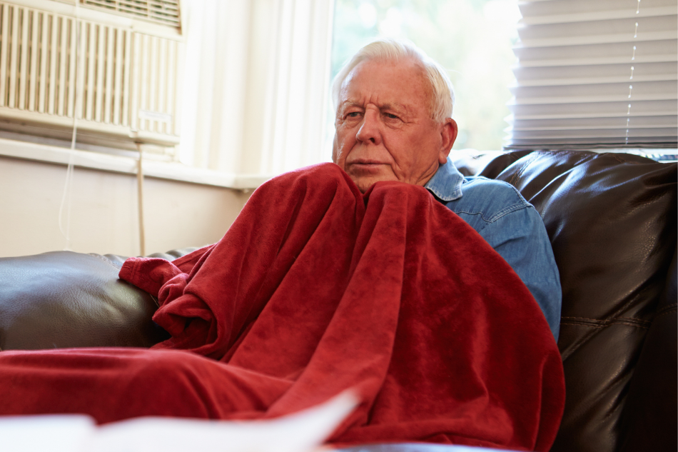 Elderly man freezing in living room and pulling red blanket tight to him