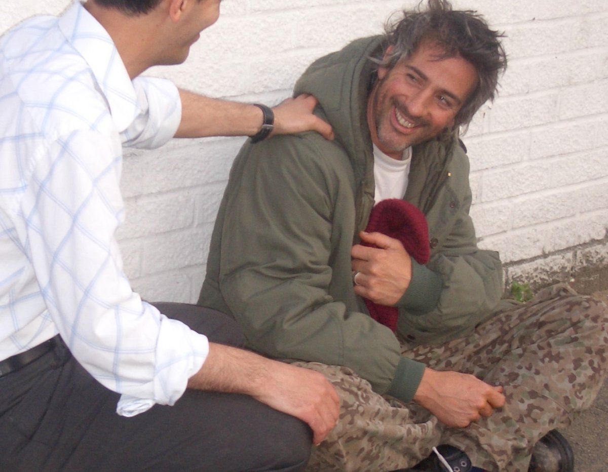 Homeless man in army fatigues sitting on ground and smiling at a volunteer