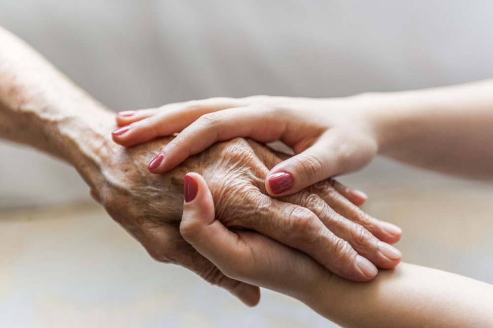 Two hands holding an elderly persons hand in comfort.