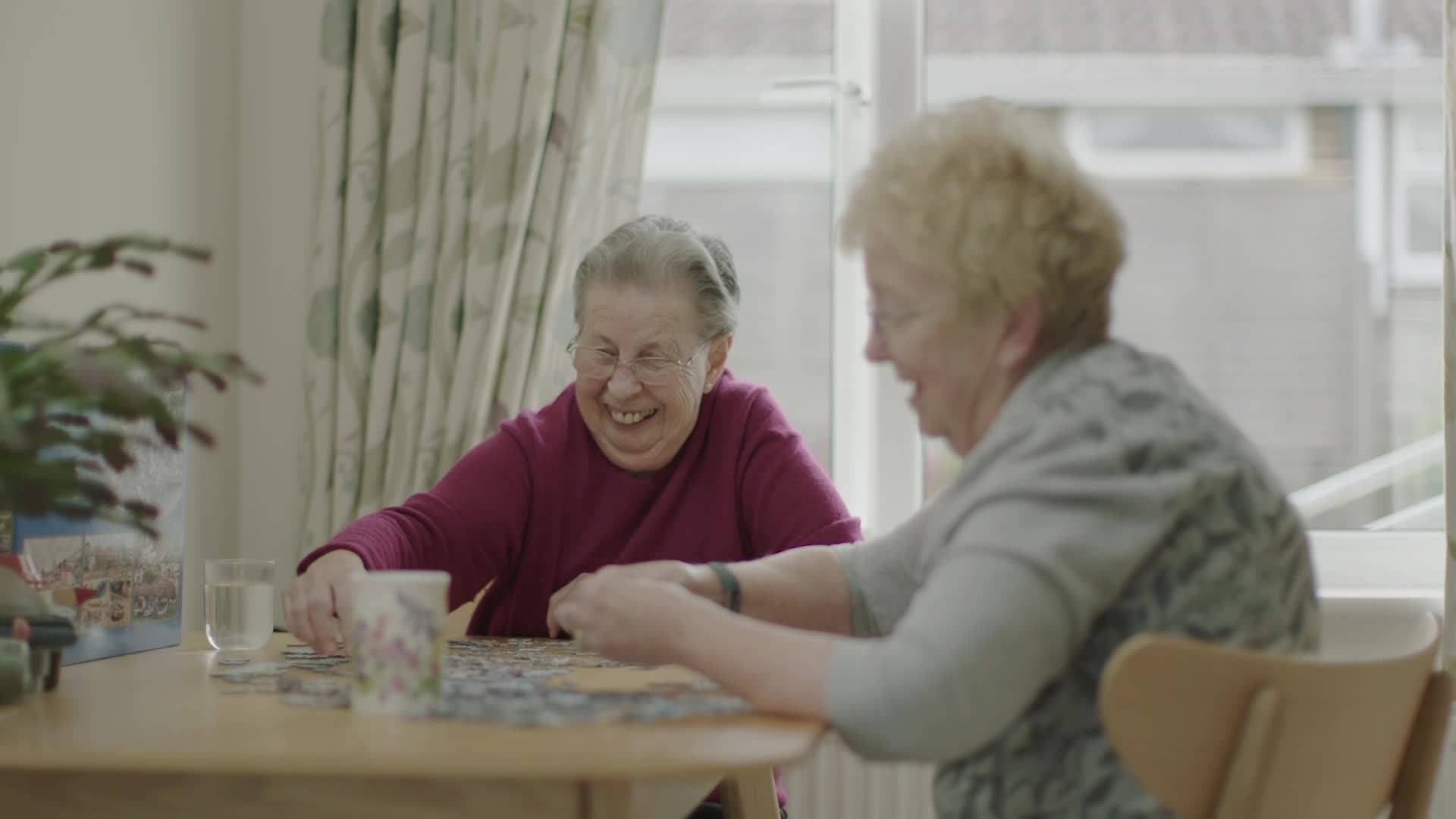 Ann and Mary sit together at a table putting together a jigsaw